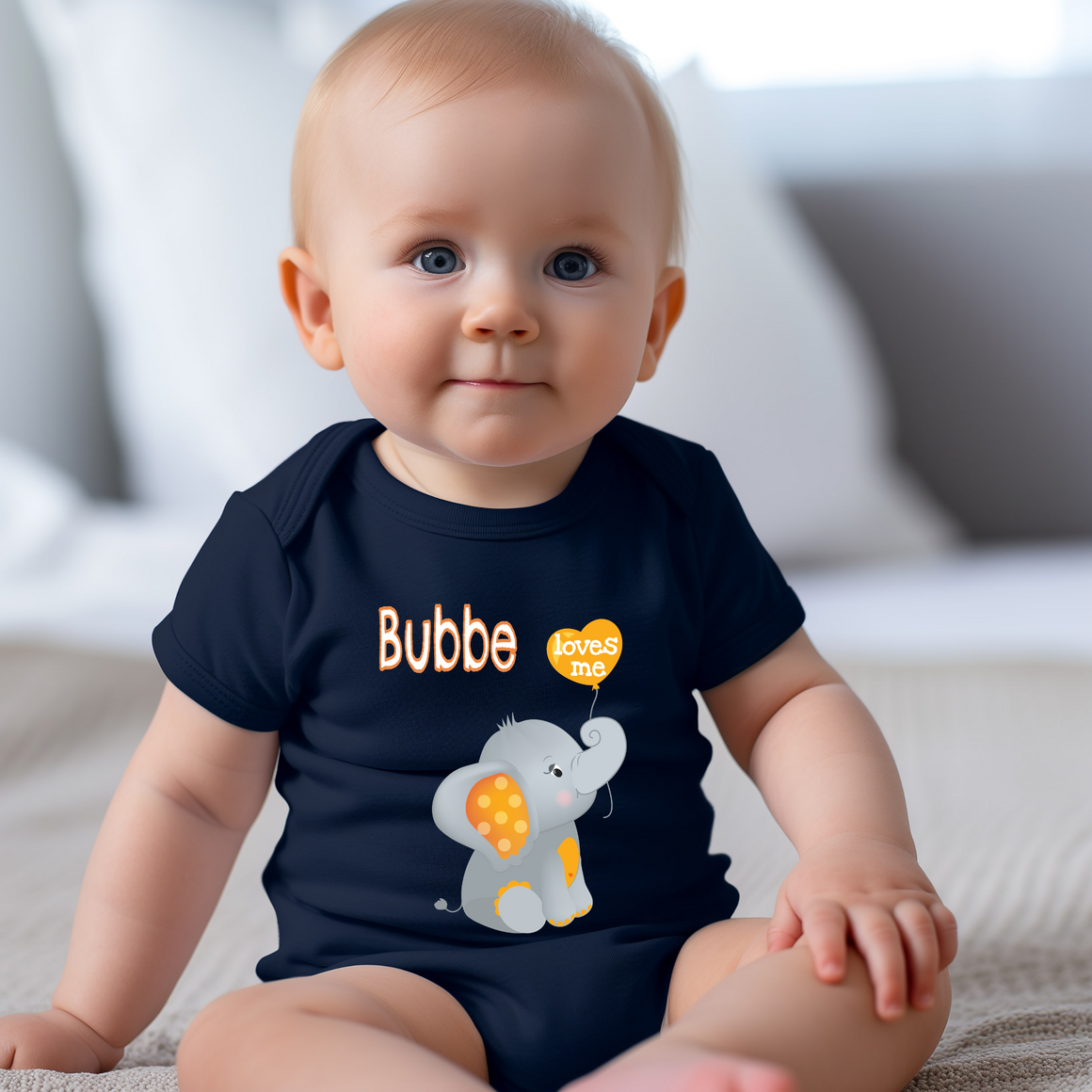 A smiling baby boy wearing a navy blue t-shirt with an elephant graphic and the text " Bubbe loves me" printed on it.