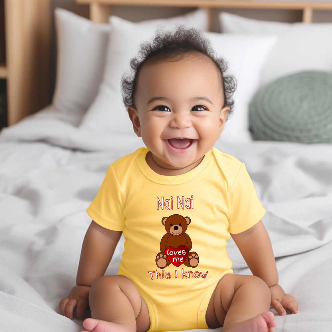 A smiling baby wearing a yellow onesie with a teddy bear graphic and text.