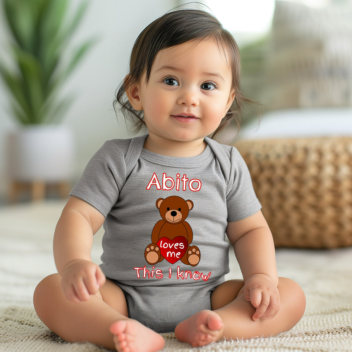 A smiling baby girl wearing a gray onesie with a teddy bear graphic and text.