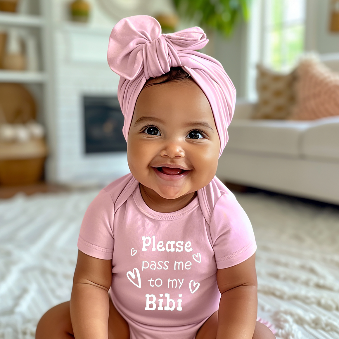 A smiling baby girl wearing a pink outfit with a bow on her head and a t-shirt with the text "Please pass me to my Bibi" is sitting on a white rug in a living room.