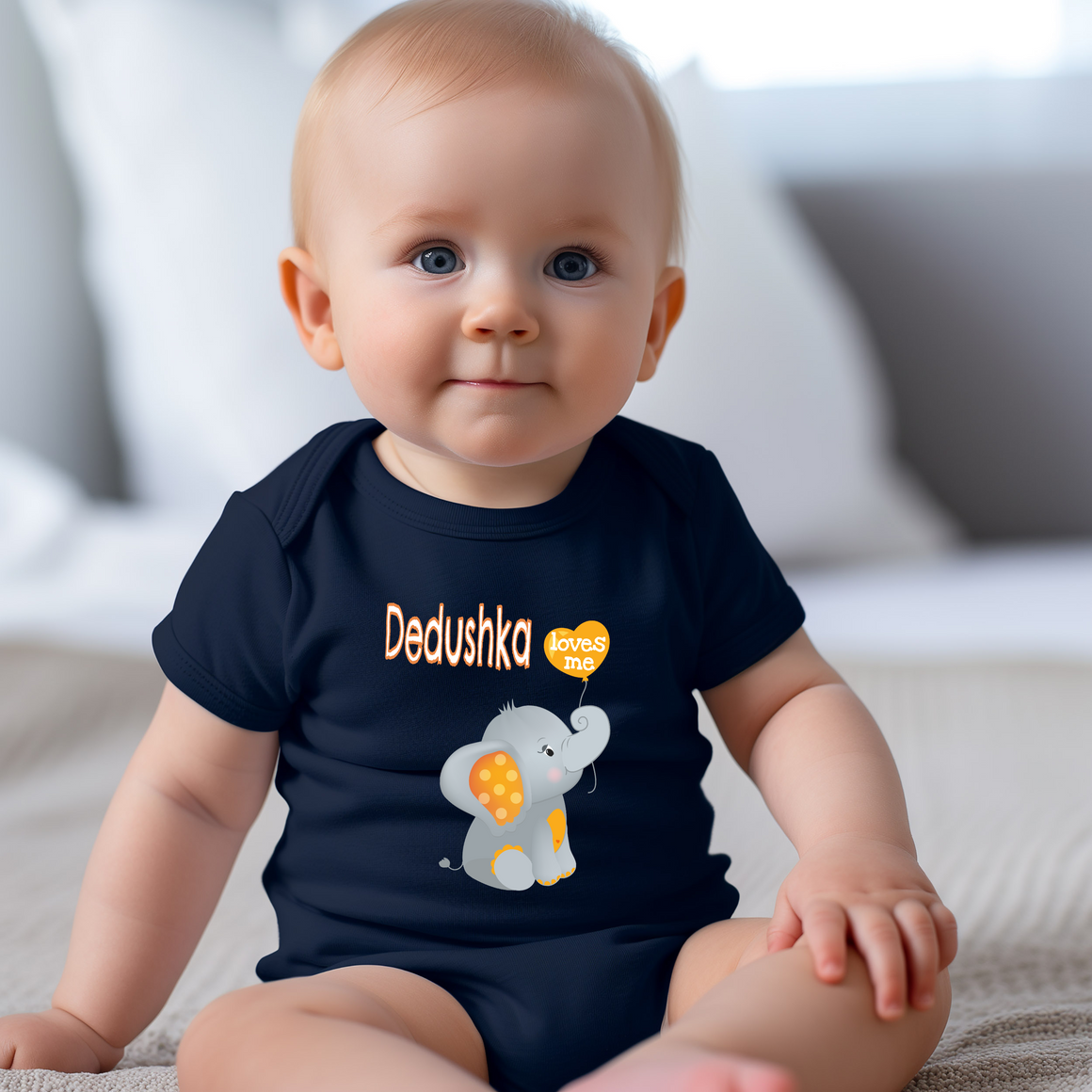 A smiling baby boy wearing a navy blue t-shirt with an elephant graphic and the text "Dedushka loves me" printed on it.
