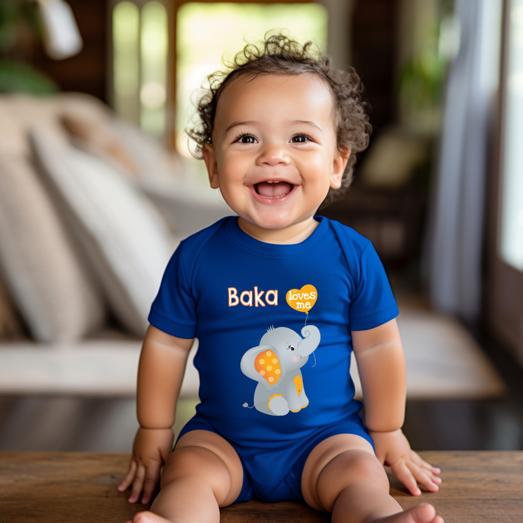 A smiling baby boy wearing a blue onesie with an elephant design sits on a wooden surface.