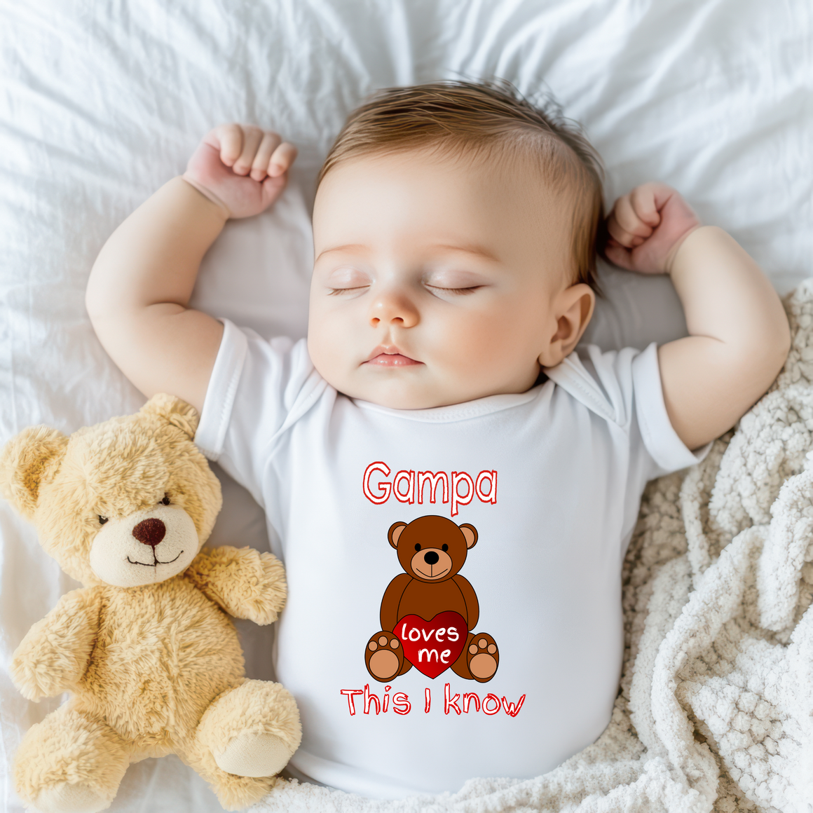 A sleeping baby wearing a white onesie with a teddy bear next to them.