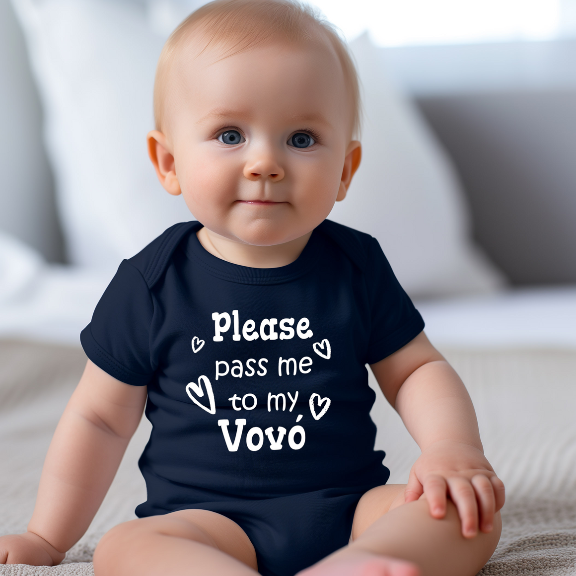 A smiling baby wearing a navy blue onesie with the text "Please pass me to my Vovo" printed on it.