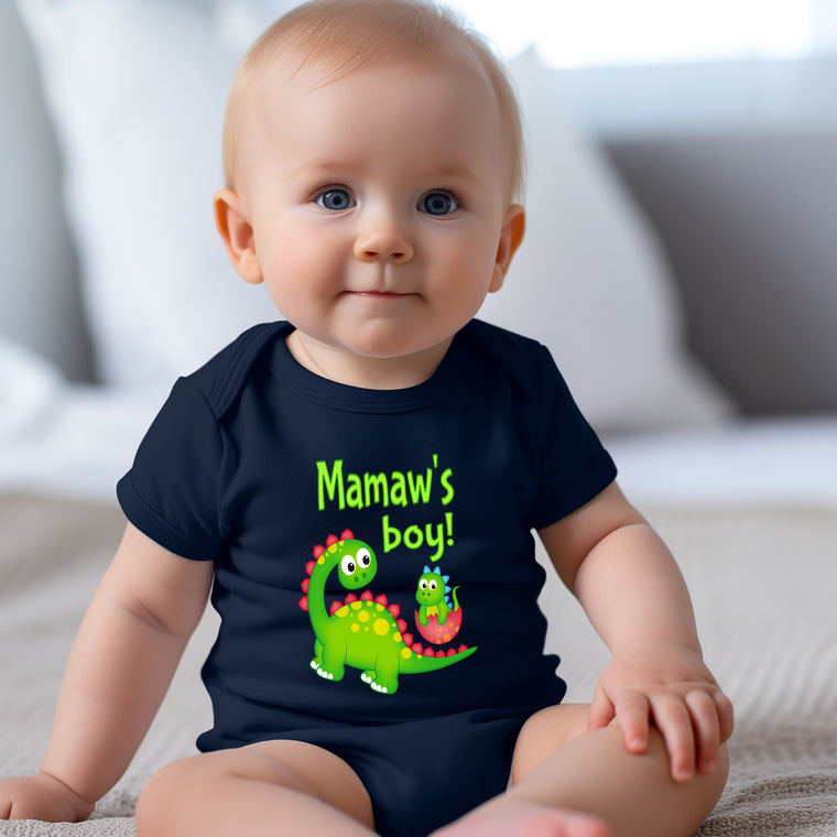 A smiling baby wearing a black t-shirt with a dinosaur graphic and text that says "Mamaw's boy!"