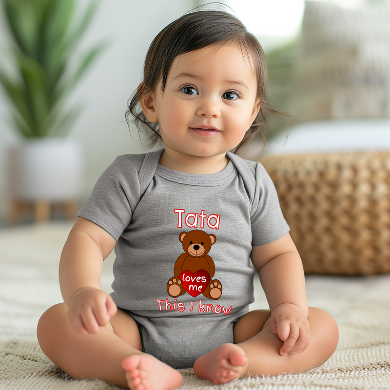 A smiling baby girl wearing a gray onesie with a teddy bear graphic and text.