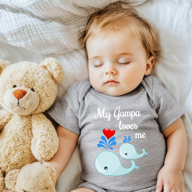 A sleeping baby wearing a gray onesie with a teddy bear and a whale graphic, accompanied by the text "My Gampa loves me".