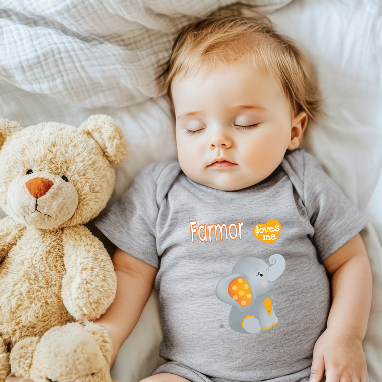 A sleeping baby wearing a gray shirt with an elephant and the word "Farmer" printed on it, lying next to a stuffed teddy bear.