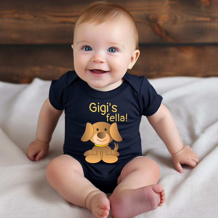 A smiling baby wearing a black shirt with a cartoon dog and the text "Gigi's fella!"