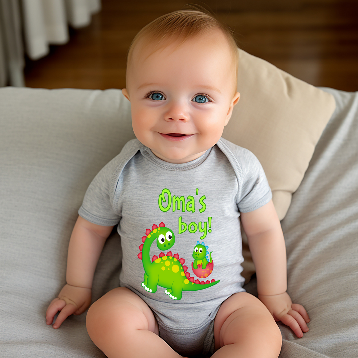 A smiling baby wearing a gray onesie with a dinosaur design and the text "Oma's boy!"