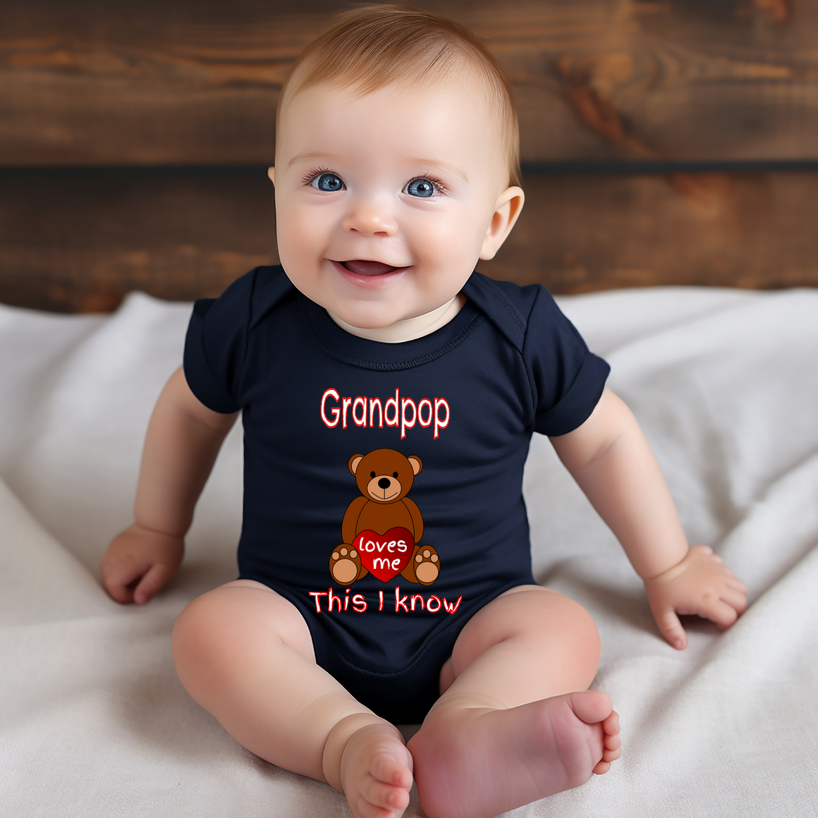 A smiling baby wearing a black t-shirt with a teddy bear graphic and text that says "Grandpop loves me This I know".