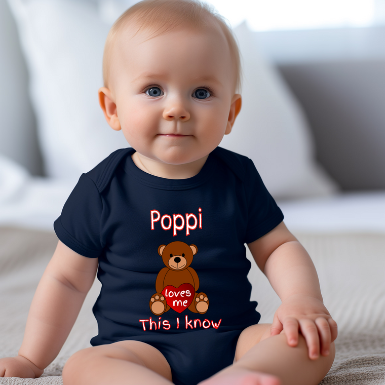 A smiling baby wearing a navy blue t-shirt with a teddy bear graphic and text that says "Poppi loves me This I know".