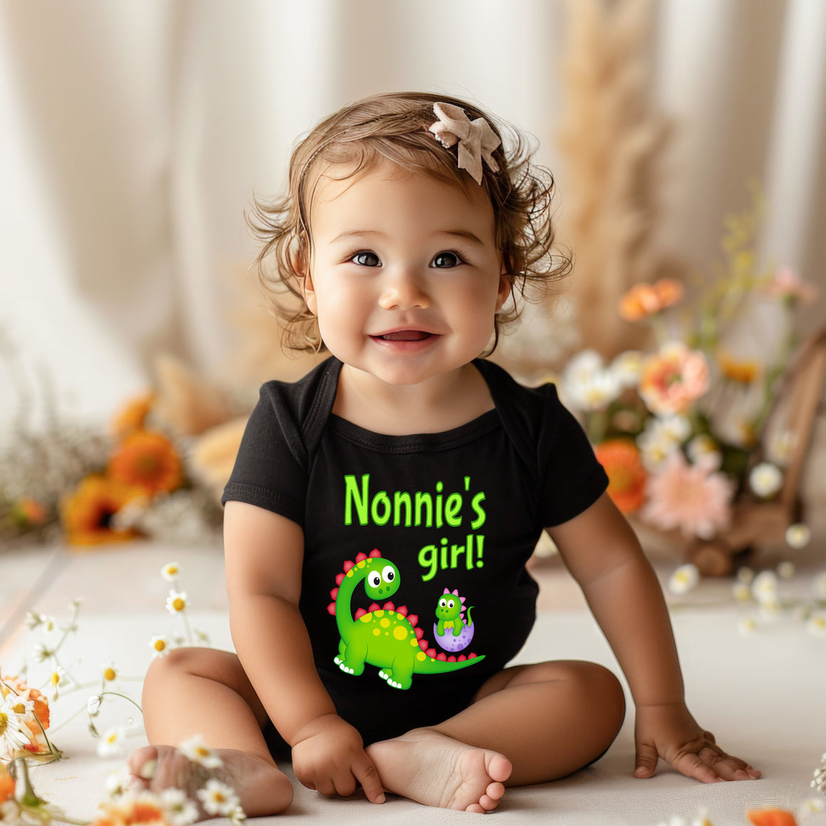 A smiling baby girl wearing a black t-shirt with a dinosaur and the text "Nonnie's girl!"