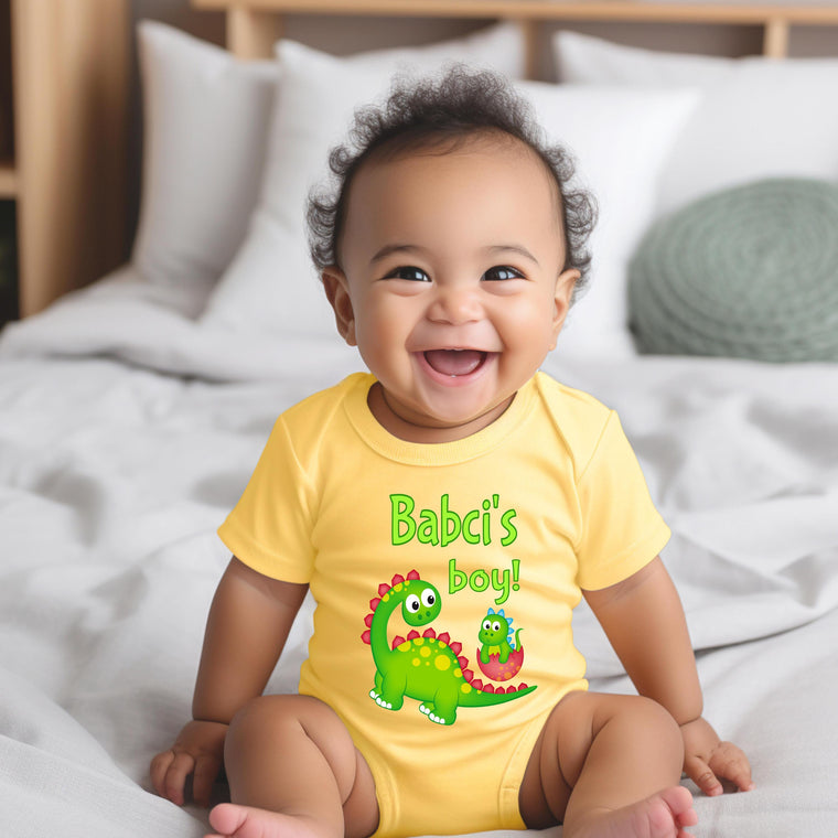A smiling baby wearing a yellow t-shirt with a dinosaur graphic and text.
