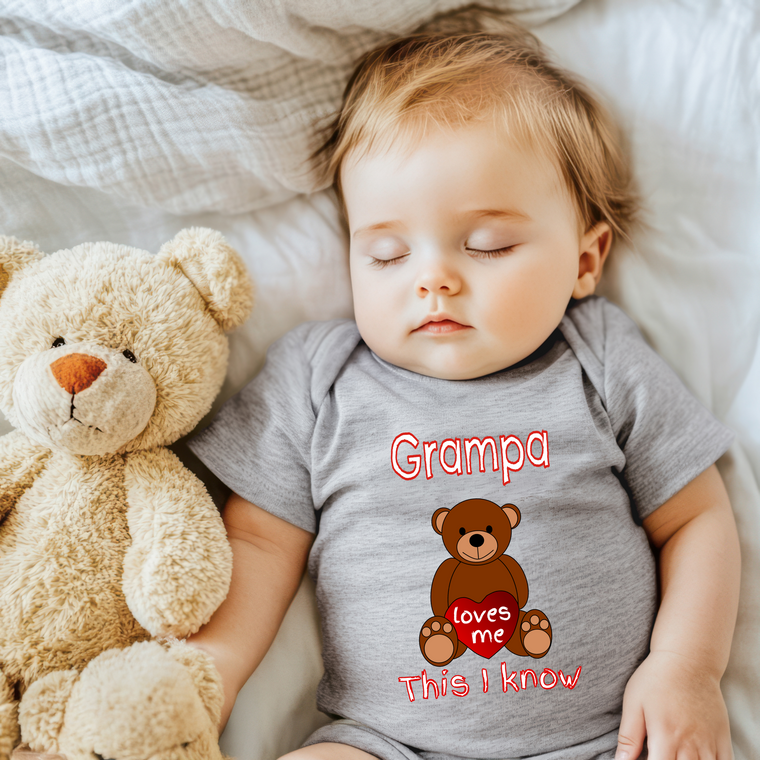 A sleeping baby wearing a gray shirt with a teddy bear and the text "Grampa loves me this I know" printed on it.
