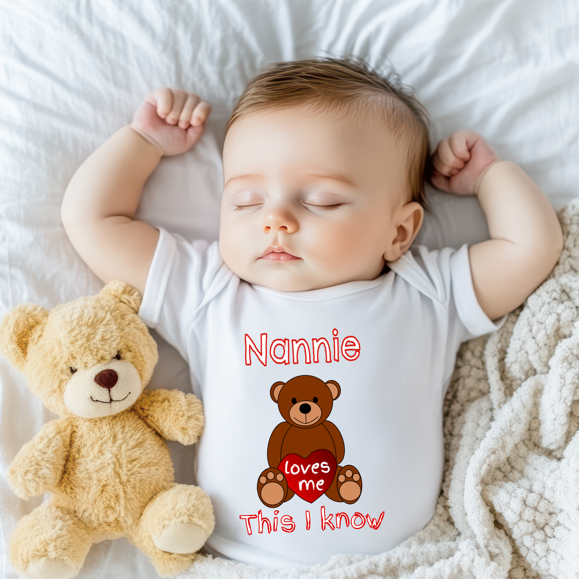 A sleeping baby wearing a white onesie with a teddy bear and the text "Nanny loves me" printed on it.