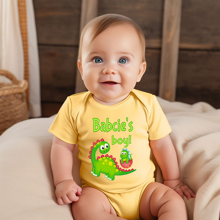 A smiling baby wearing a yellow onesie with a dinosaur design and the text "Babie's boy!"